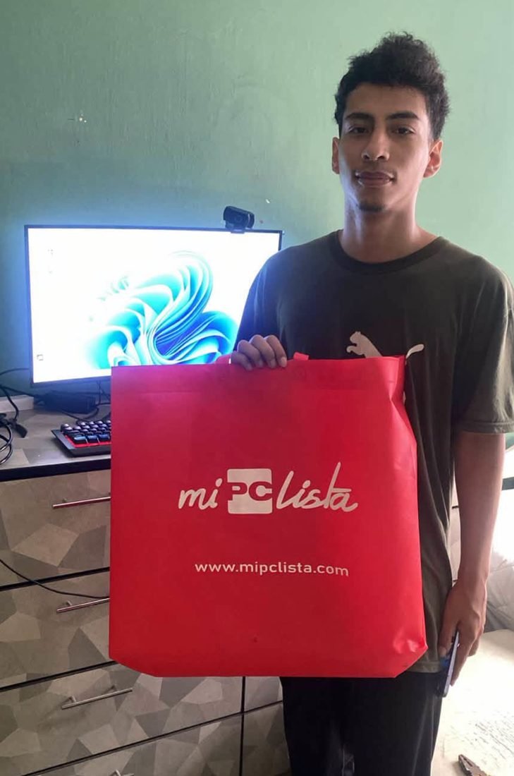 Cliente con su compra junto a una PC instalada en la tienda